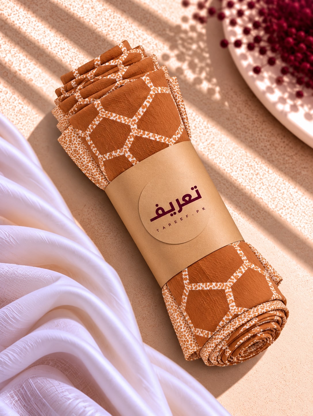 A terracotta brown hijab with a cream geometric lattice pattern and matching border, styled on a white mannequin torso in a warm, sunlit interior setting.