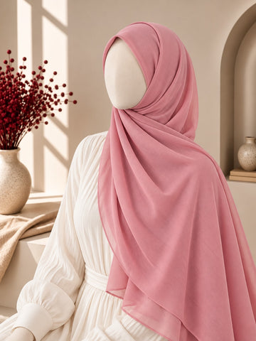 A dusty pink hijab draped elegantly on a mannequin wearing a white long-sleeve dress, set in a warm, sunlit interior with a vase of red berries on a windowsill.