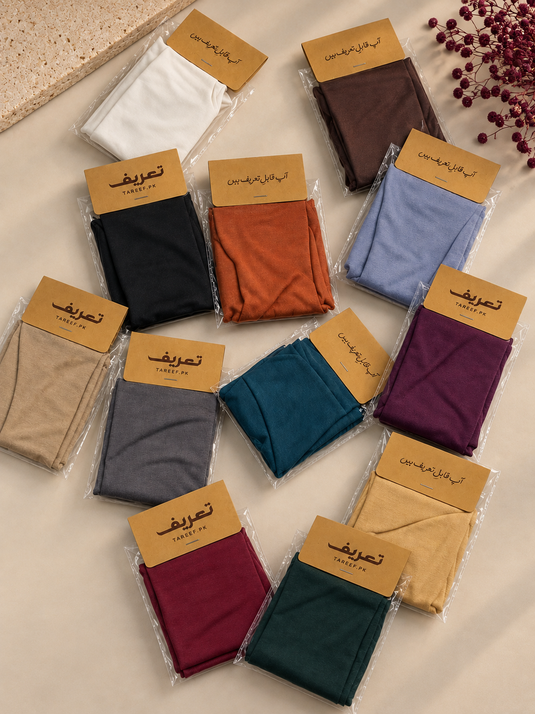 Multiple pairs of folded hijab caps in clear plastic packaging with tan paper labels, arranged on a light beige surface. The hijab caps come in several colors, including white, brown, black, orange, light blue, beige, gray, teal, purple, maroon, mustard, and dark green.