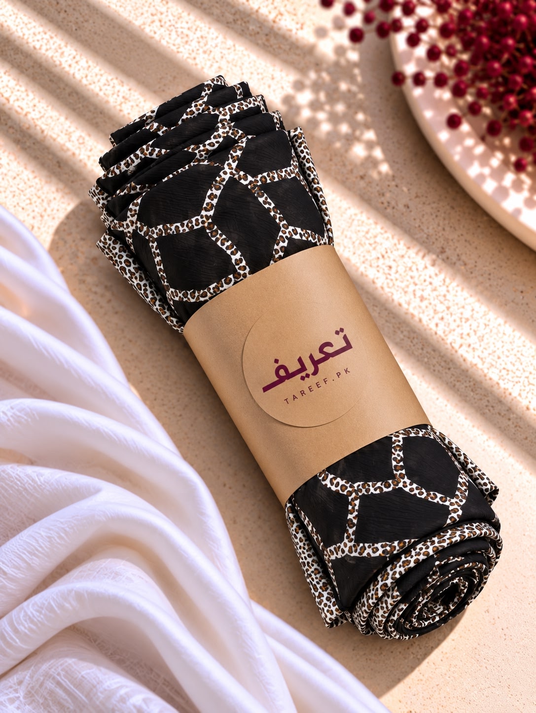 A black hijab with a silver geometric lattice pattern and a matching patterned border, styled on a white mannequin dress in a warm, sunlit interior setting.