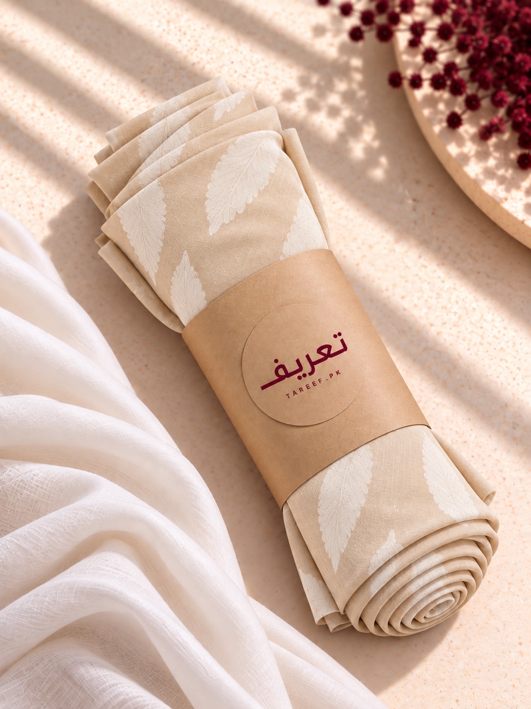 A cream-colored hijab with a white leaf pattern draped over a mannequin wearing a matching cream dress in a warm, sunlit interior setting.