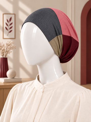 A color-blocked hijab tube displayed on a white mannequin head, styled with a cream-colored blouse in a warm, softly lit interior setting.