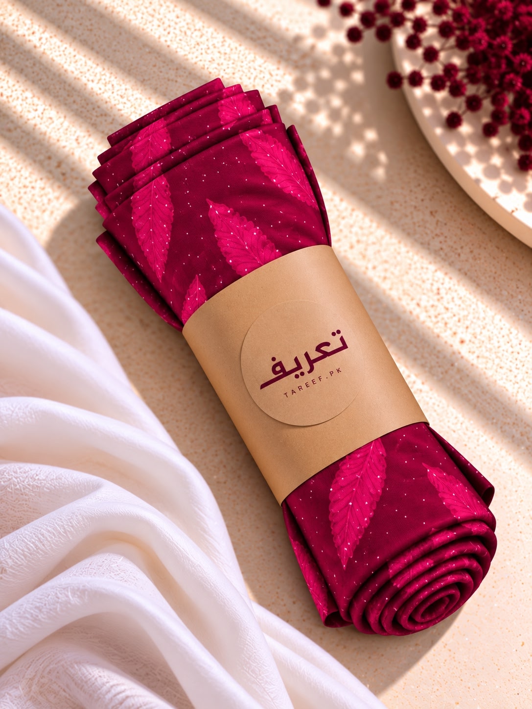 A deep magenta hijab with a leaf pattern and subtle gold glitter, styled on a white mannequin in a warm, sunlit interior setting.