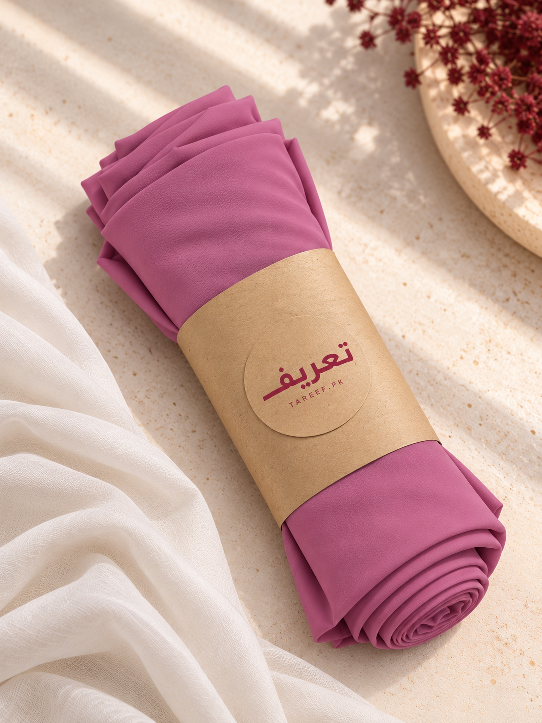 A rolled-up mauve-pink hijab, wrapped in a brown kraft paper band with the brand name 'TAREEF'.