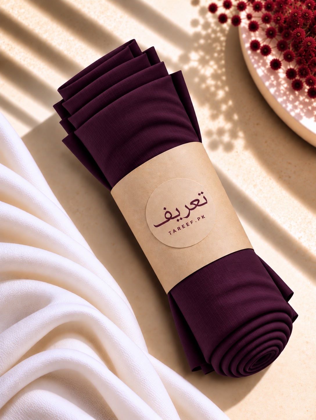 A rolled-off deep plum purple hijab wrapped in a beige paper band with the brand name 'TAREEF'.