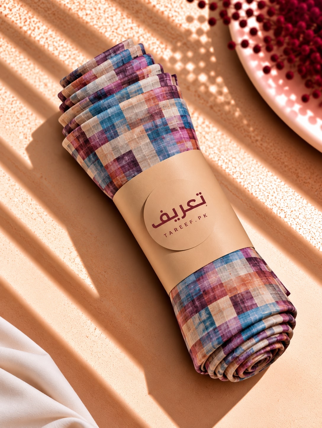 A multicolor plaid and chevron patterned hijab draped on a white mannequin wearing a cream dress, set in a warm, sunlit interior with decorative vases.