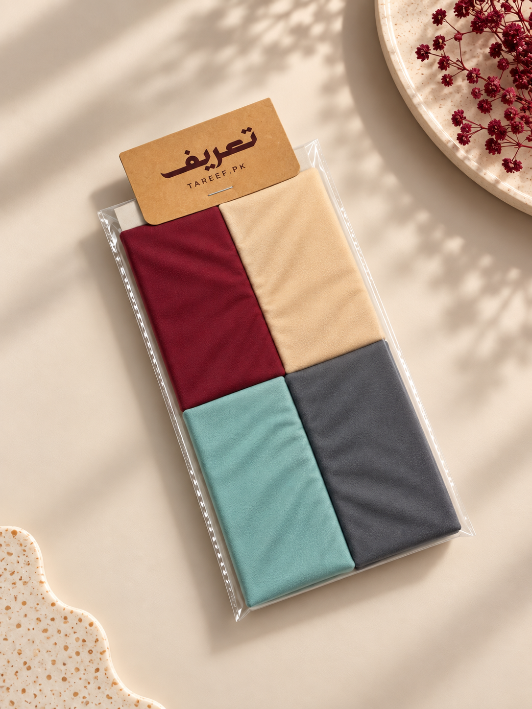 A packaged hijab tube in four different colors: burgundy, beige, mint green, and charcoal gray, presented on a beige background with decorative shadows and dried flowers.