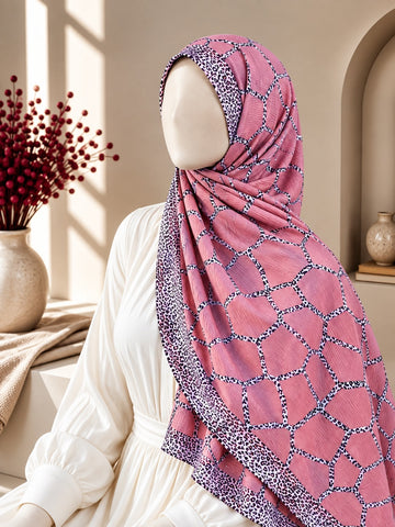 A pink patterned hijab draped on a mannequin wearing a white dress, set in a warm, sunlit interior with decorative red berries in a vase and a beige wall arch.