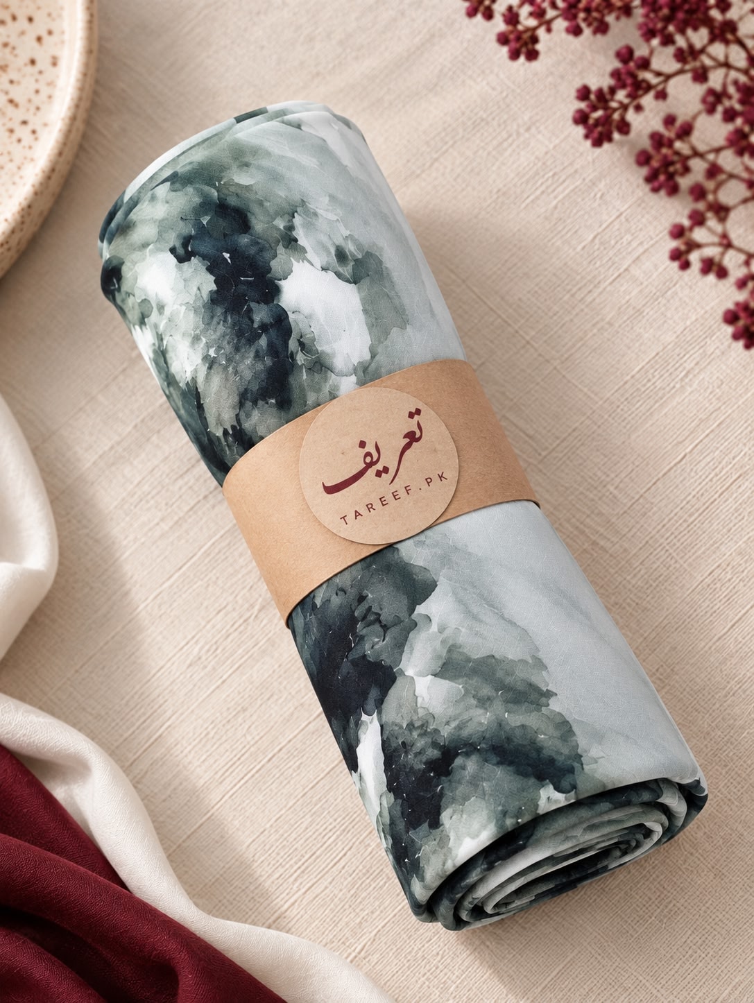 A draped hijab with a watercolor-style abstract print in shades of light blue, gray, and black, styled on a mannequin wearing a white dress in a warm, sunlit interior setting.