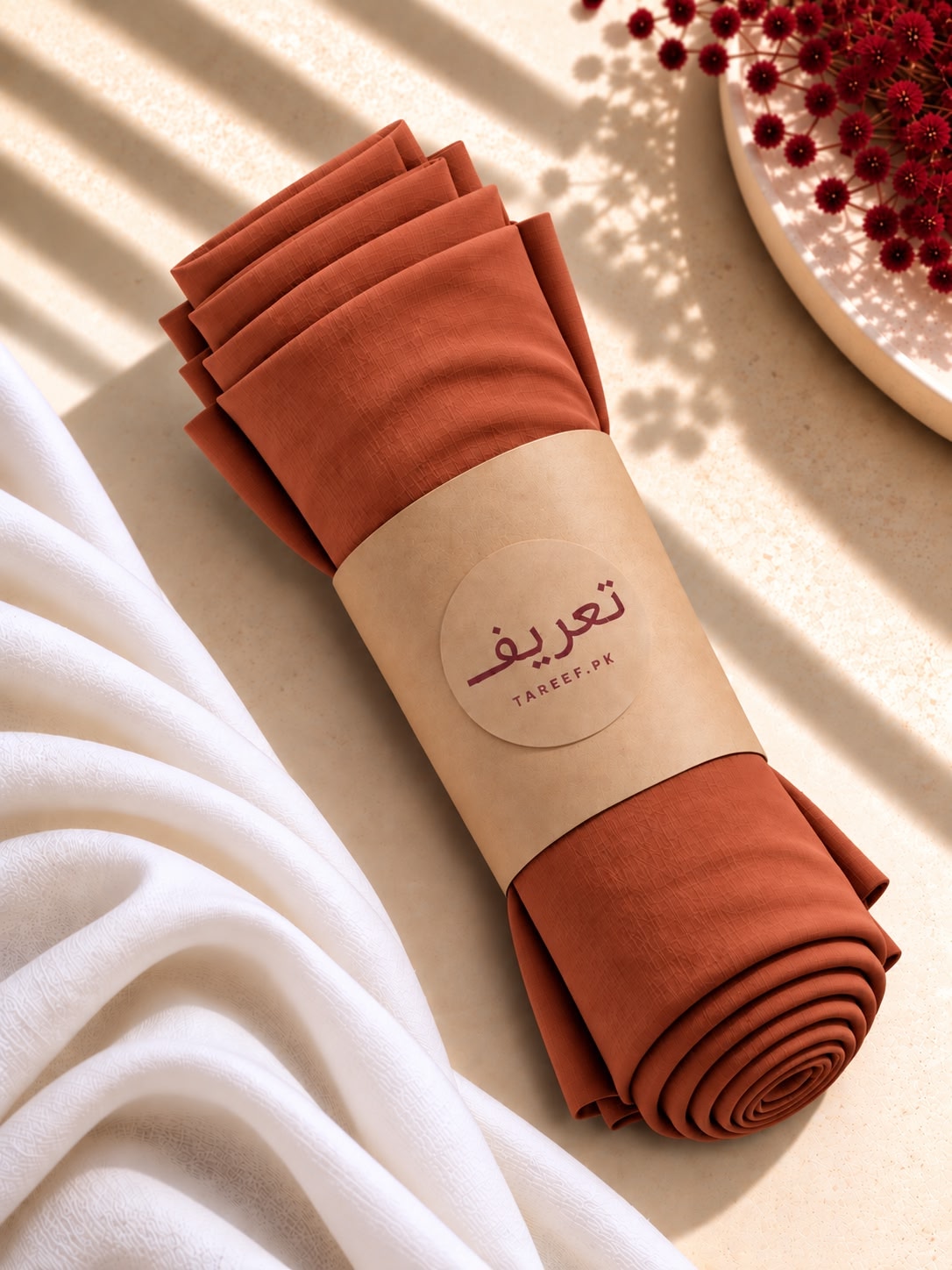 A draped terracotta rust-colored hijab styled on a white mannequin wearing a white dress, set in a warm, sunlit interior with decorative vases.