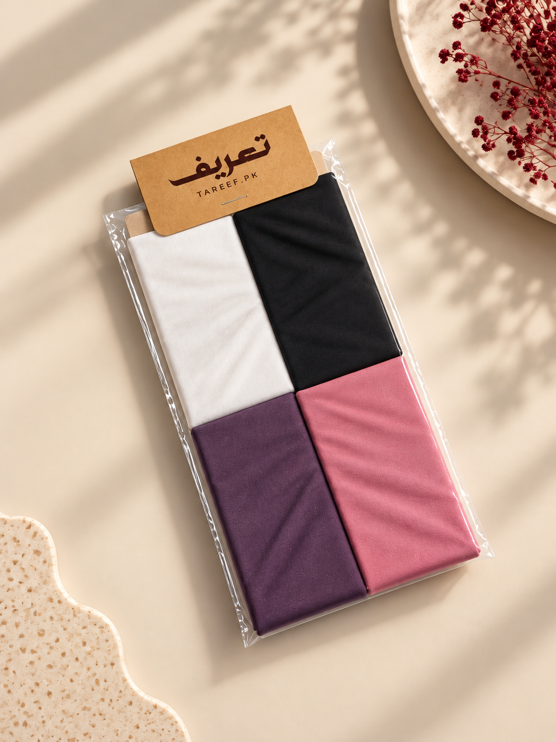 A four-color color-blocked hijab tube in purple, pink, and black, styled on a white mannequin head wearing a cream-colored blouse in a warm, softly lit indoor setting.