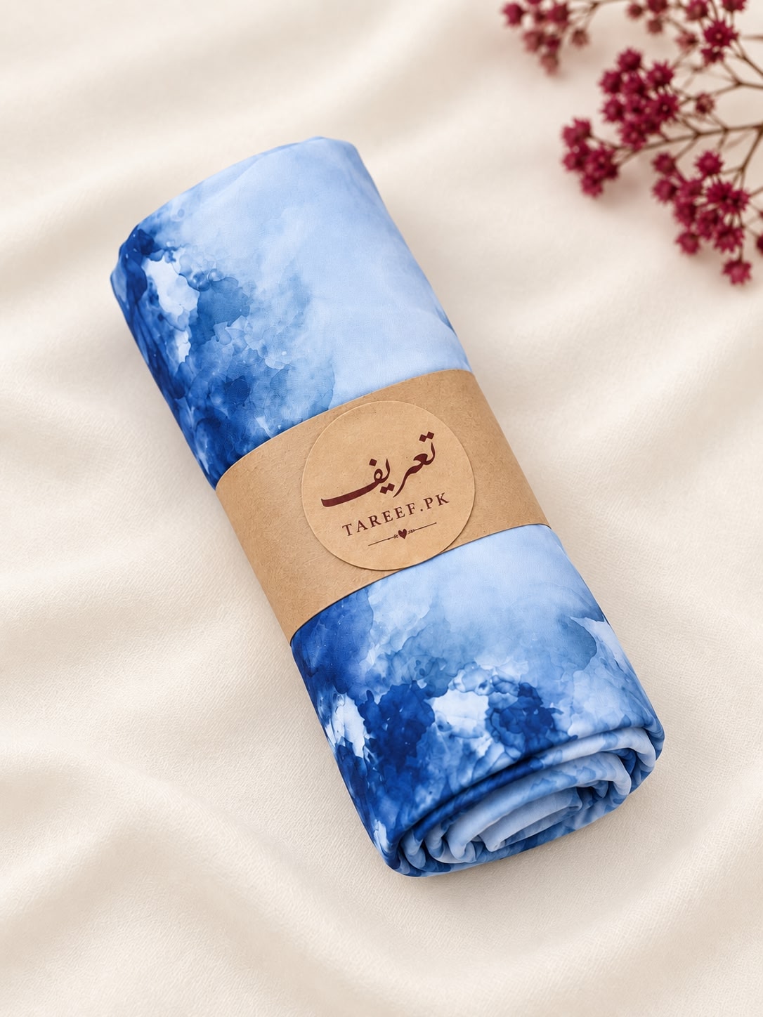 A light blue and navy watercolor-patterned hijab draped on a white dress form mannequin in a warm, sunlit interior setting.