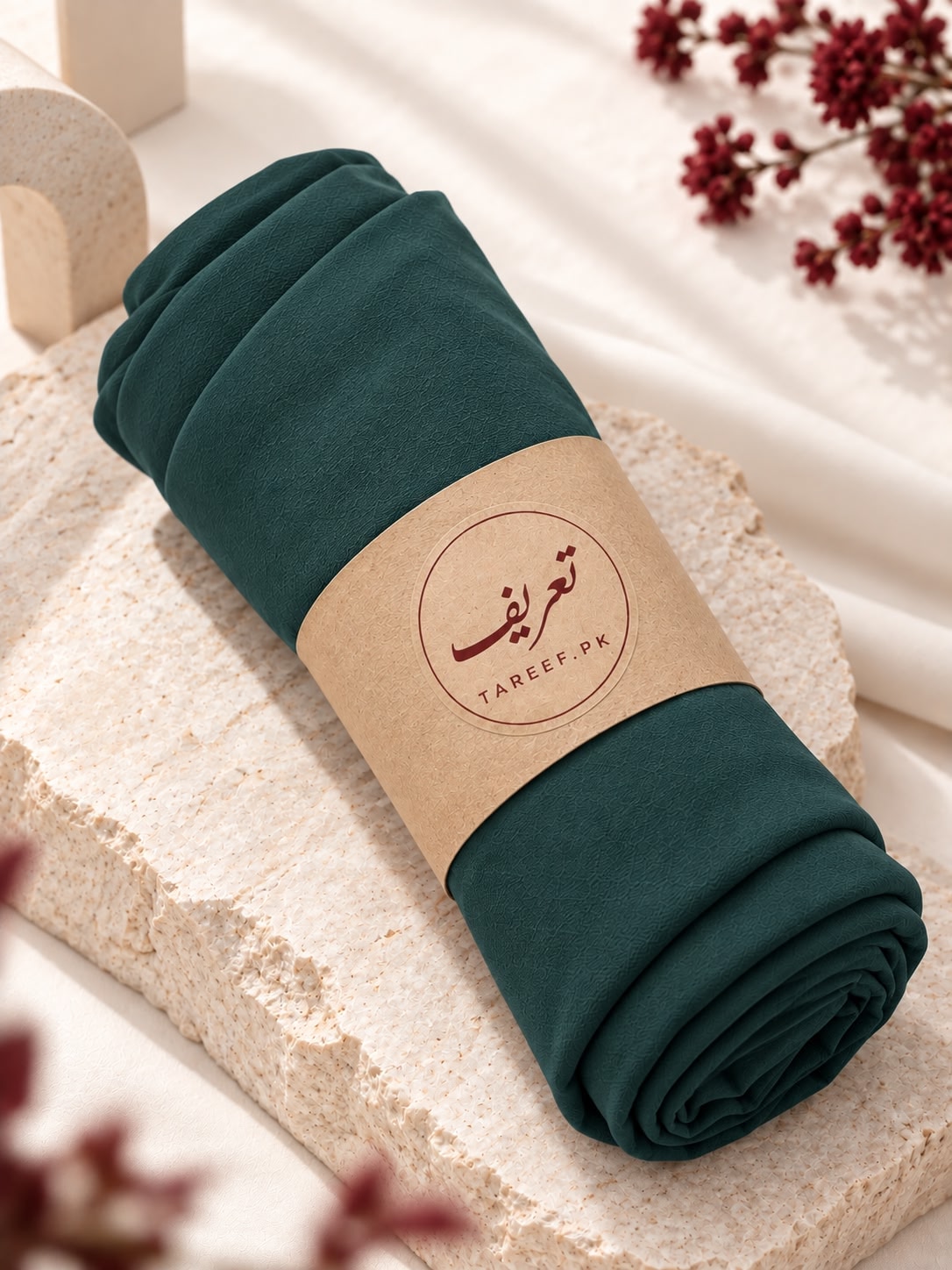 A rolled dark teal-green hijab wrapped in a kraft paper band with the brand name 'TAREEF.' printed on it.